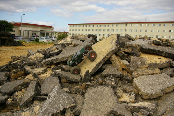 Green remote control car climbing a pile of broken asphalt and concrete