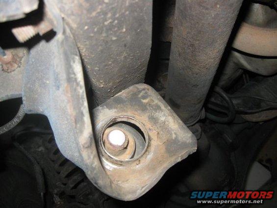 Undercarriage view of a vehicle's suspension mount with a bolt. Visible text: SUPERMOTORS www.supermotors.net
