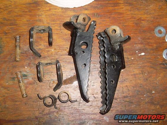 Two motorcycle foot pegs, springs, and mounting hardware laid out on a wooden surface