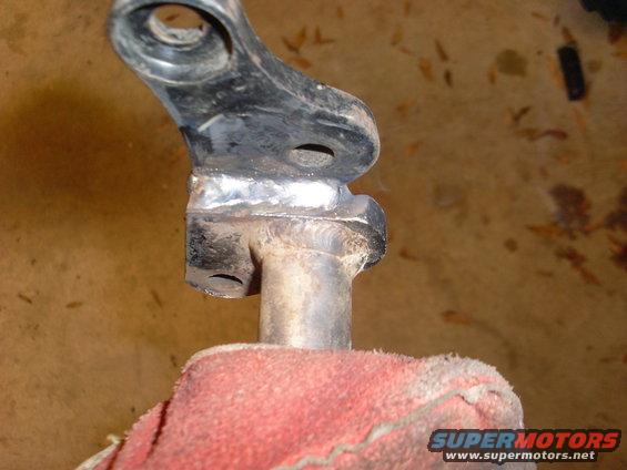 close-up of a metal bracket with fresh welds, held by a red glove