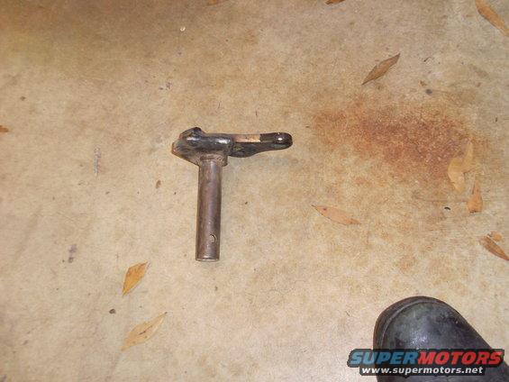 Metal part with a cylindrical base and a lever arm, lying on a concrete floor with scattered leaves