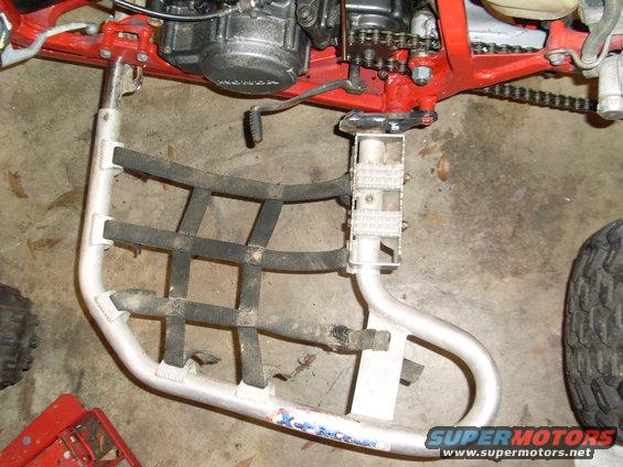Close-up of an ATV's aluminum footpeg with netting and part of the engine visible