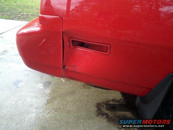 Close-up of damaged red car rear bumper with a broken turn signal housing