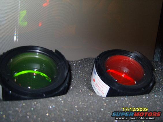 Two vehicle lights, one green and one red, sit on a textured surface