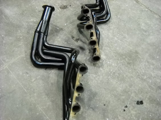 Two black exhaust manifolds with four pipes each, lying on a concrete floor