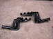 1978 Ford Bronco - Two sets of black exhaust headers are laid out on a concrete surface.