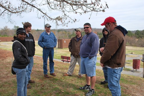 Group of people standing in an outdoor area with trees and some structures in the background