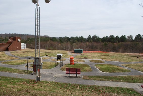 Clay shooting range with multiple throwing stations, a tall tower with lights, and a wooded background
