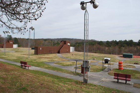 Outdoor shooting range with clay targets, benches, and lighting towers under a cloudy sky