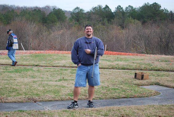 Man with shotgun at skeet range, another person in background