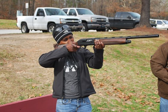 Woman aiming a shotgun with trucks in the background