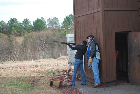 Two people at a shooting range, one aiming a rifle, the other observing