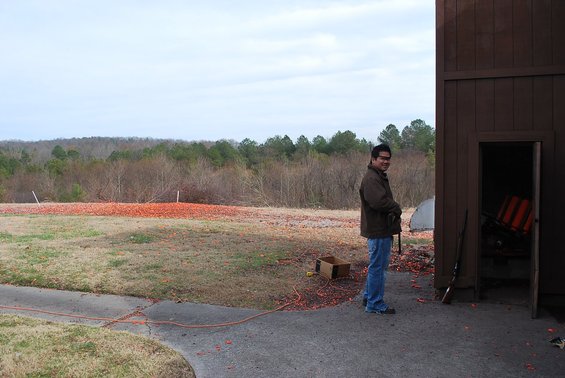 man standing next to a building at a shooting range, with clay targets scattered on the ground