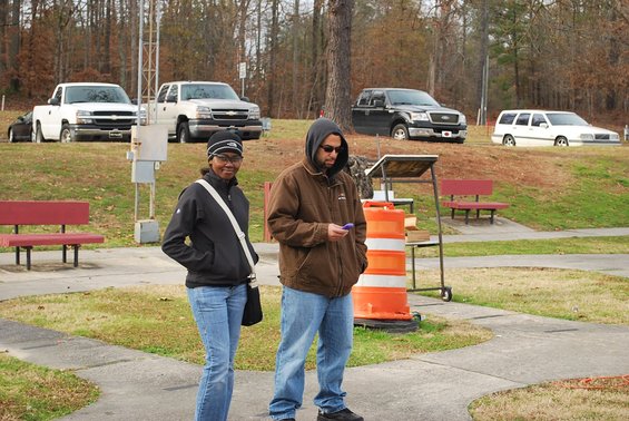 Two people stand in front of several parked trucks and a station wagon