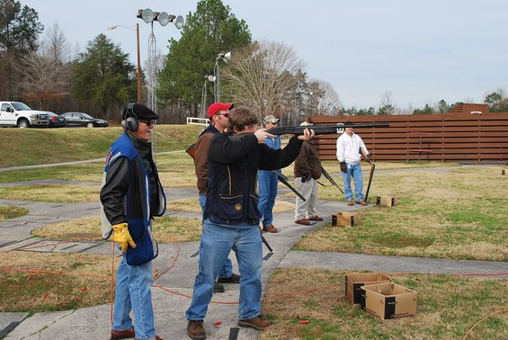 People at a shooting range, one person aiming a shotgun at clay pigeons