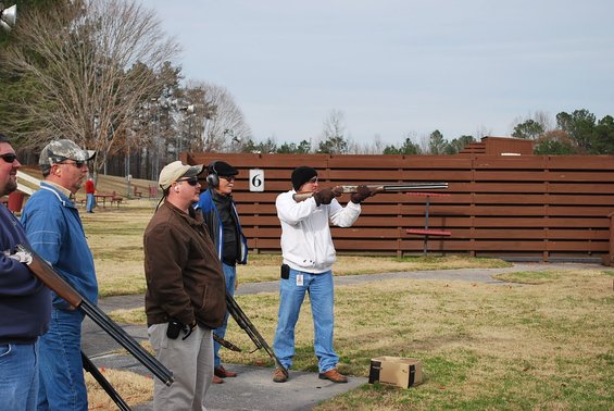 Men with shotguns at a shooting range, one aiming