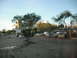 1991 Ford Bronco - A view of a parking lot with several vehicles, trees, and buildings in the background, under a bright sky.