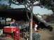1991 Ford Bronco - A street taco stand is set up under a large black tarp, with a red cooler and water jugs nearby.