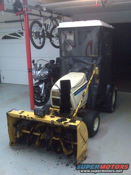 Yellow snowblower with cab and a motorcycle in the background