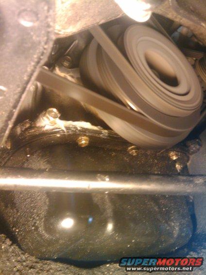 Engine belt wrapped around pulleys, with oil pan visible below
