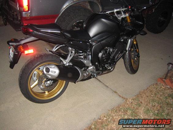 Black motorcycle with gold wheels parked next to a truck