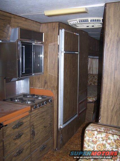 RV interior showing a four-burner stove, oven, refrigerator, and seating area