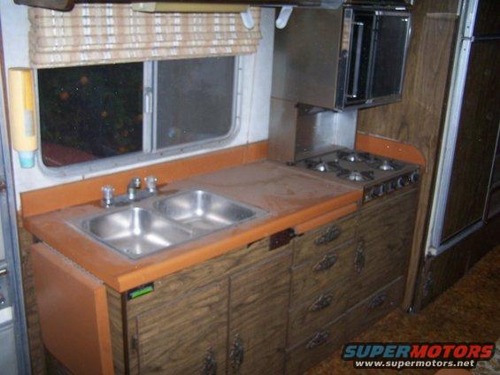 RV interior kitchen area with double sink, orange countertop, and gas stove