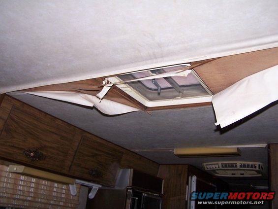 RV interior with damaged ceiling panel near skylight and wood cabinets