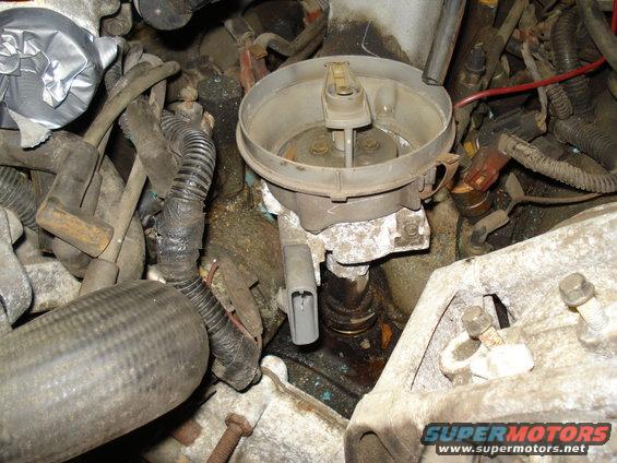Engine distributor cap with wires, some duct tape on hoses, and visible corrosion