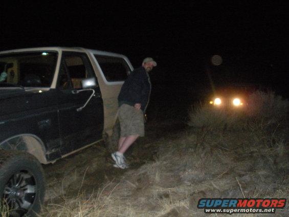 Black and tan 1990 Ford Bronco parked at night with a person standing by the open door