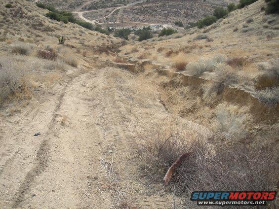 Dirt road with tire tracks descending a dry, eroded hillside with sparse vegetation