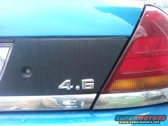Close-up of a blue car's rear with a black panel and '4.6' badge. Chrome trim below