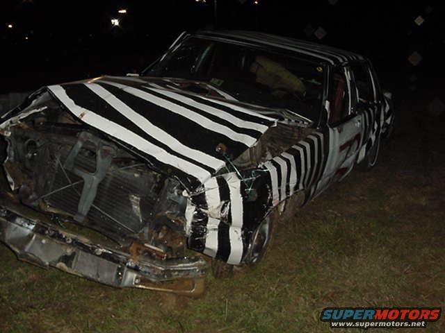 Damaged car with black and white zebra stripes, front end crushed, parked on grass at night