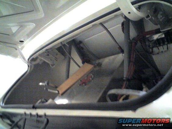 Inside of a car trunk, showing hinges, wiring, and some metal bracing