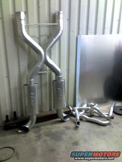 Dual exhaust system with mufflers and bent pipes, leaning against a wall
