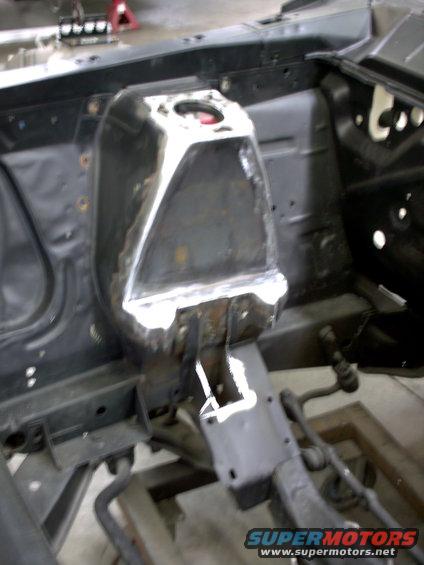 Car's engine bay with modified shock tower and suspension components visible. Some welding work is apparent