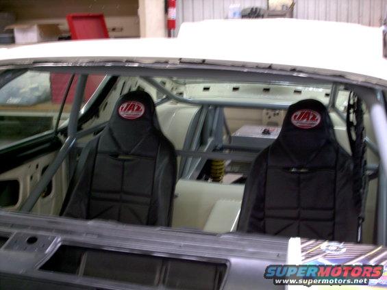 Interior of a car with two black JAZ racing seats, roll cage, and exposed metal dashboard