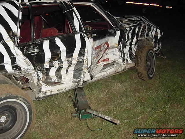 Demolition derby car with zebra paint, damaged, on a jack