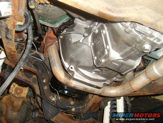 Underside view of a vehicle's transmission and exhaust pipes. Lots of rust on the frame