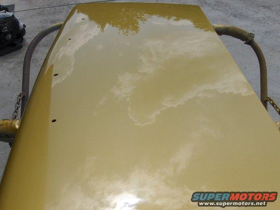 Yellow car hood with reflections of clouds and trees. Holes drilled in the surface