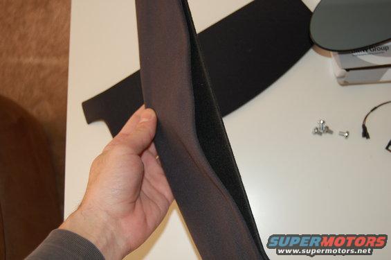 Hand holding a dark grey car interior trim piece with velcro on the back. Some screws and a wire are on the table