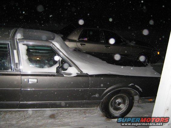 Dark hearse covered in snow, parked next to another car