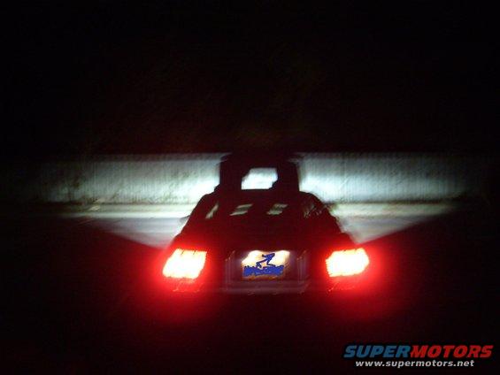 Rear view of a dark vehicle with taillights illuminated at night. A license plate is visible
