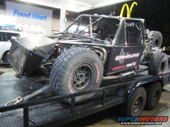 Black off-road buggy with roll cage and large tires on a dual-axle trailer