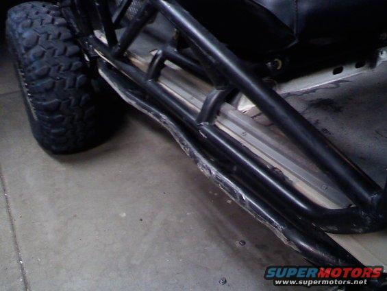Close-up of a large off-road tire and black roll cage tubing, showing some damage on the lower tube