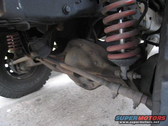 Close-up of a vehicle's front axle, steering linkage, and red coil springs