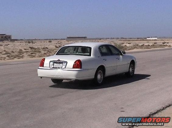 White sedan driving on a road. Looks like a Lincoln Town Car