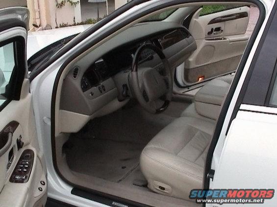 Front passenger seat and dashboard of a white car. Light tan leather seats and carpet. Wood trim on doors and dash