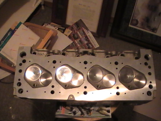 Close-up of an aluminum engine cylinder head with valves visible. Text 'BUICK' is stamped on top
