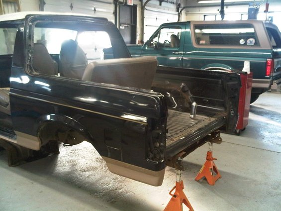 Black Ford Bronco rear section on jack stands, with a green Ford Bronco behind it